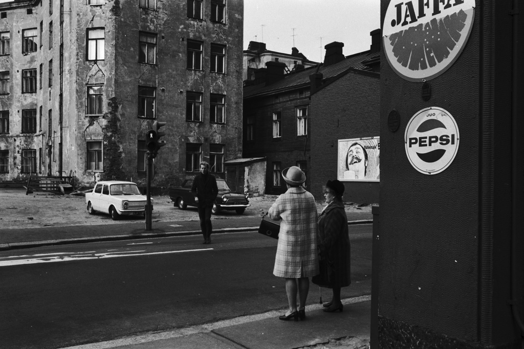 Kaksi naista seisomassa liikennevaloissa Ruoholahdenkadulla Abrahaminkadun kulmassa, mies ylittämässä katua