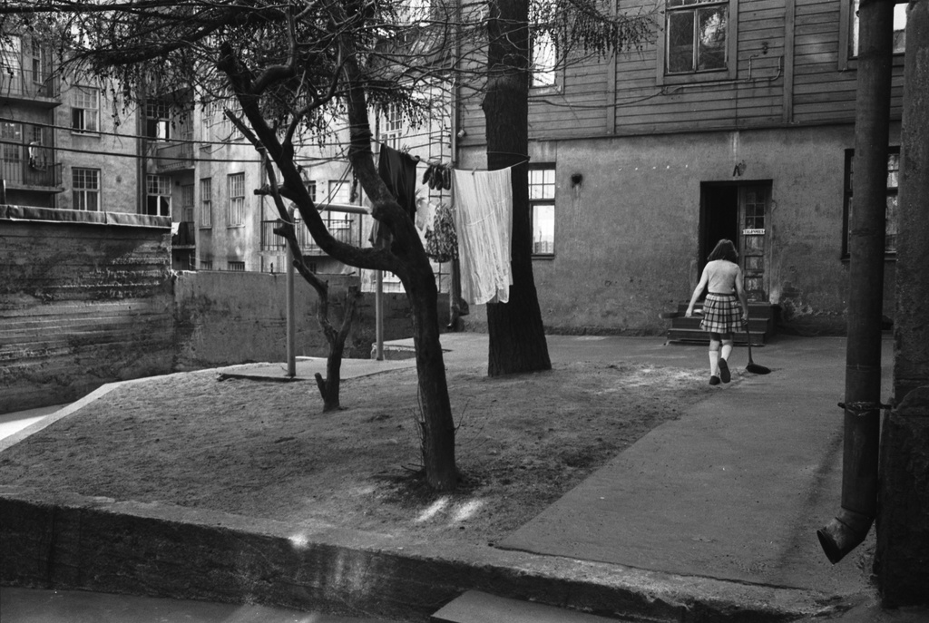 Saariniemenkatu 6. Tyttö lakaisemassa lattiaharjalla Saariniemenkatu 6:n pihaa, jossa pyykkiä kuivumassa