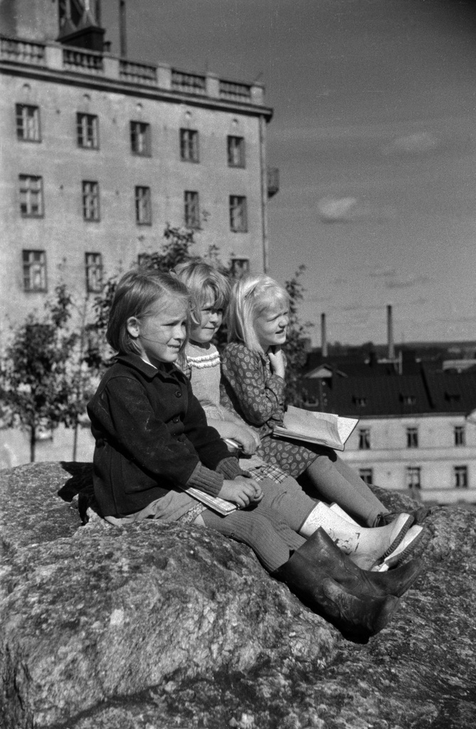 Kolme tyttöä istumassa kallioilla Katri Valan puistossa, takana Vilhonvuorenkuja 20.
