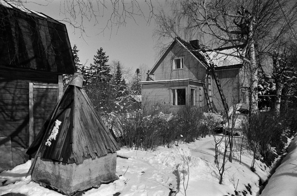 Luminen puutaloalue, jossa kaivoja talojen pihalla pääsiäisen kevätauringossa Pukinmäen Savelassa. Kevättalvi 1974.