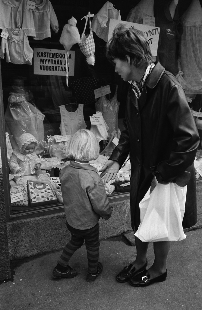 Hämeentie 6. Äiti lapsineen vaateliikkeen näyteikkunan edessä.