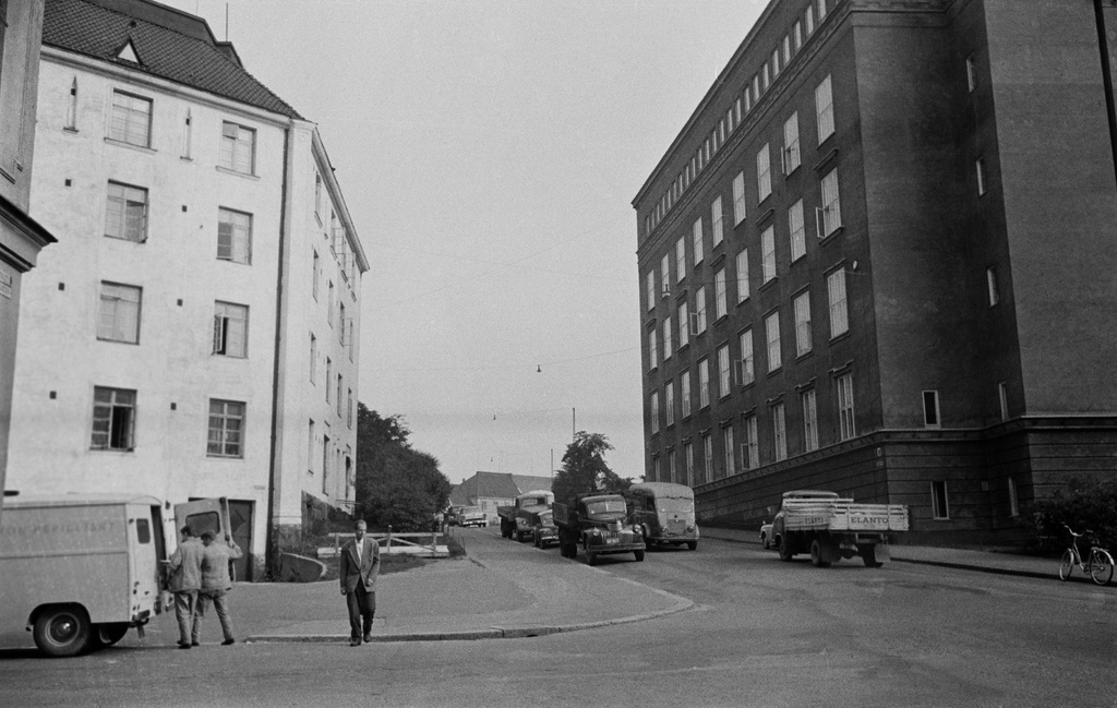 Katunäkymä, vasemmalla Torkkelinkatu 19 (Agricolankuja 1), oikealla Helsingin teknillinen oppilaitos (Agricolankatu 3-1). Vasemmalla F. Heinon perillisten tukkuliikkeen pakettiauto ja työntekijöitä, oikealla Elannon kuorma-auto.
