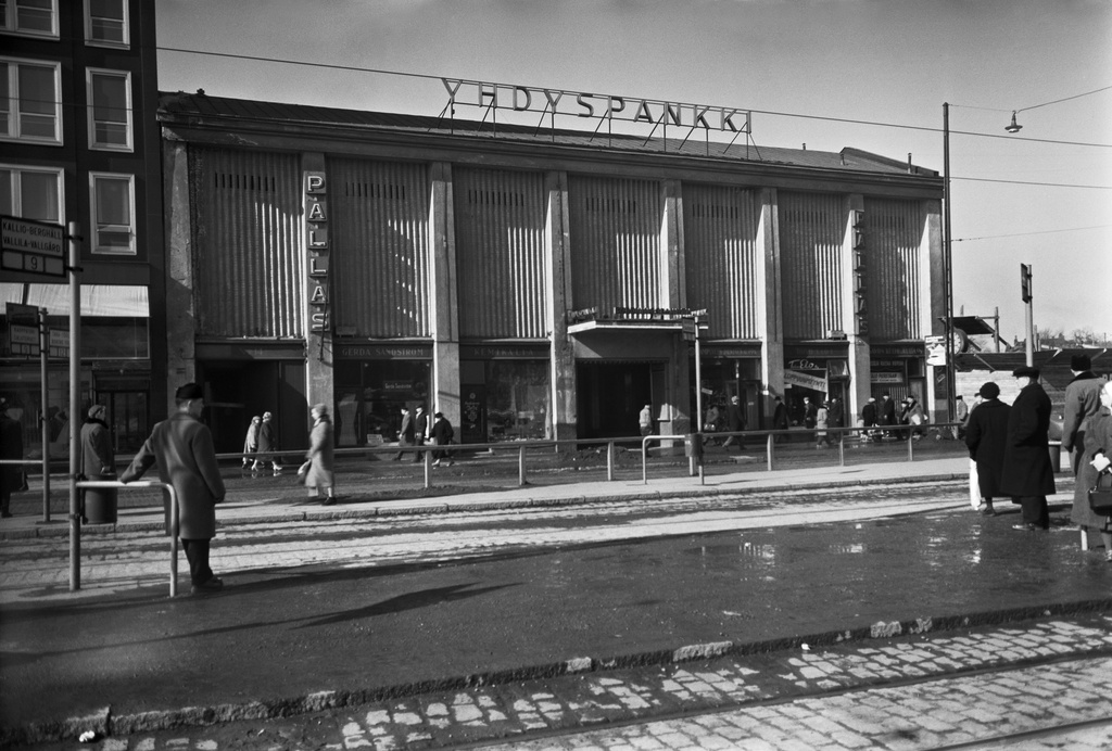 Siltasaarenkatu 14. Yhdyspankki, Pallas -elokuvateatteri, katutasossa useita liiketiloja, joiden ikkunoissa mm. kyltit 'loppuunmyynti' ja 'talo puretaan'. Talo purettu 1958. Kadun varressa raitiovaunujen 9 ja 12 pysäkit.