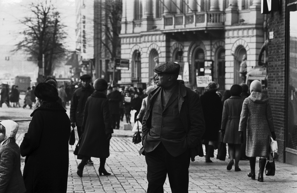 Kluuvi, Mannerheimintie 1. Lippalakkipäinen mies tupakka suussa ja kädet taskussa muiden jalankulkijoiden joukossa Stockmannin tavaratalon kulmalla Mannerheimintiellä.