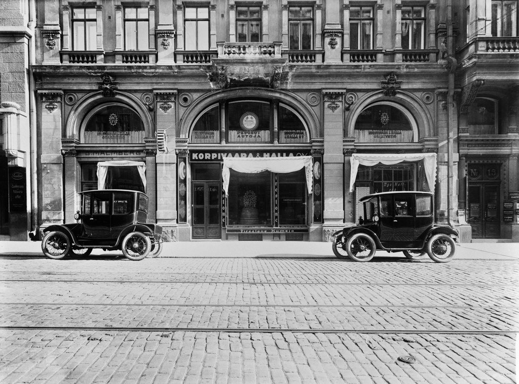 Autoja Aleksanterinkatu 15:ssa, taustalla Korpivaara & Halla Oy. Autot ovat Korpivaaran tuomia amerikkalaisia, sähkökäyttöisiä Rauch & Lang -merkkisiä autoja. Hallan historiikin mukaan näitä tuotiin nämä kaksi kappaletta, sillä polttoaineesta oli pulaa sisällissodan kynnyksellä. Ajoneuvoja myytiin Helsingin Sanomissa Baker -merkkisinä vuonna 1920.