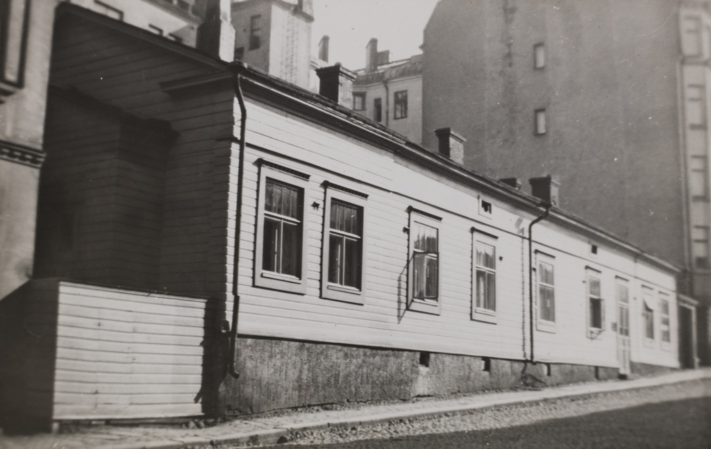 Tarkk'ampujankatu 13. Matala puutalo korkeampien kerrostalojen keskellä. Tämän talon tilalle ei purkamisen jälkeen ole rakennettu mitään, vaan sen kohdalla on nykyisin aidattu pieni piha-alue.