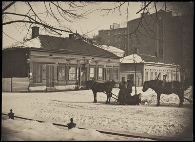 Pohjois-Esplanaadikatu (=Pohjoisesplanadi) 33 (Mikonkatu 1) ja 31 (arkkitehti Theodor Höijer, valm. 1889) talvella. Etualalla hevosrekiä, puutalossa vasemmalla suutari F. A. Loströmin liike. Puurakennuksen paikalle valmistunut 1892 Selim A. Lindqvistin piirtämä kerrostalo.  duplicate photo