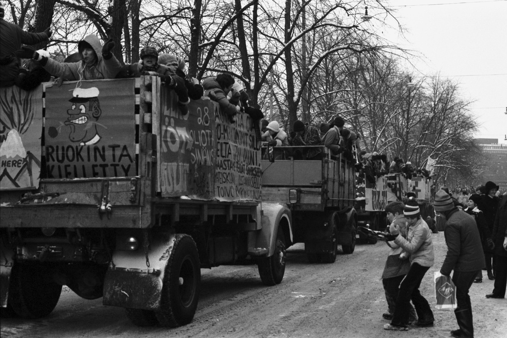 Pohjoisesplanadi. Abiturienttien perinteinen penkinpainajaispäivän ajelu. Poikia keräämässä ajoradalta plakaatein koristeltujen kuorma-autojen lavoilta heitettyjä karamelleja.