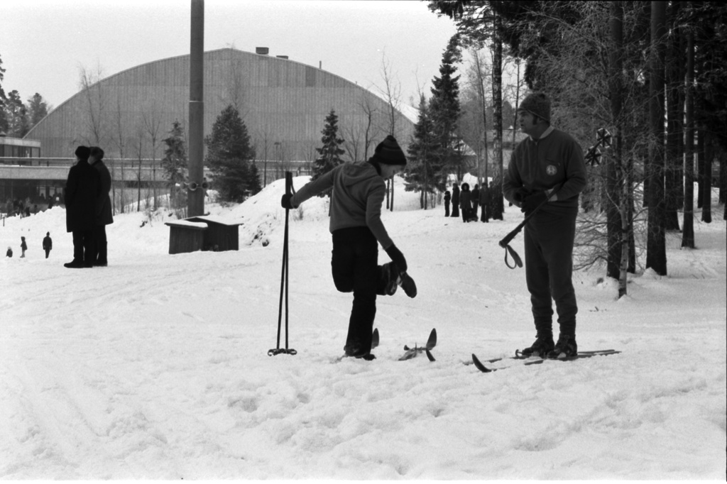Pirkkolan urheilupuisto. Ihmisiä lähdössä hiihtolenkille sekä muita ulkoilijoita Pirkkolan urheilupuistossa. Taustalla kaarevakattoinen sisäurheiluhalli.