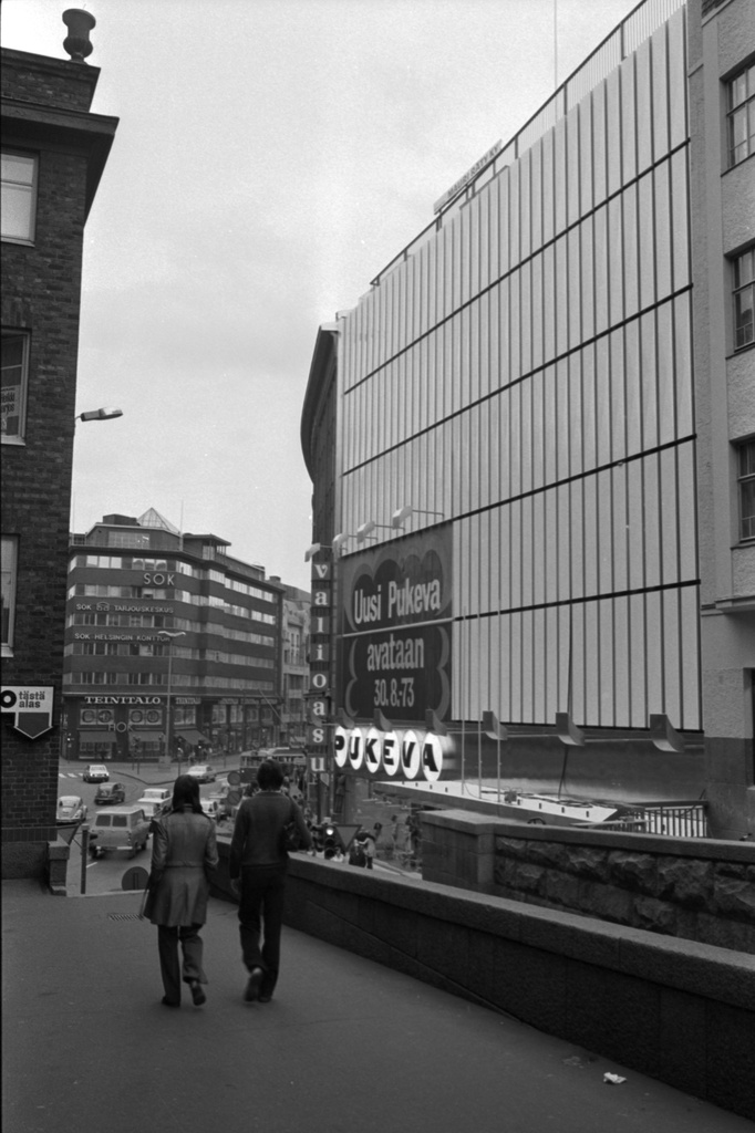 Kaisaniemenkatu 5. Pukevan tavaratalon julkisivua laajennusosan valmistuttua Vuorikatu 10:n edustalta kuvattuna. Seinässä teksti: Uusi Pukeva avataan 30.8.1973.