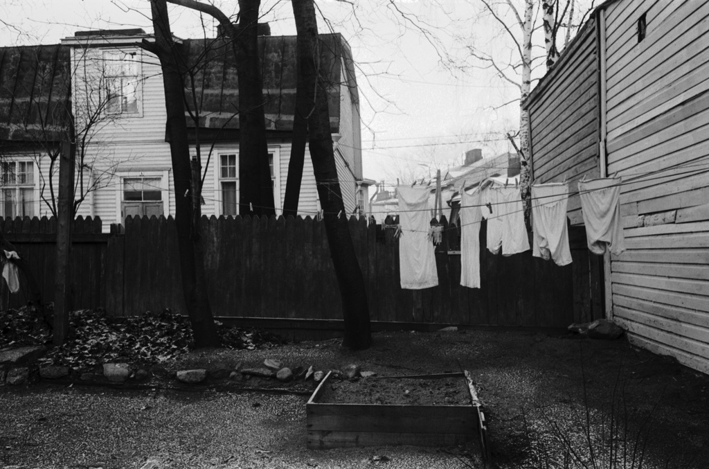 Vallila. Näkymä Päijänteentien ja Vallilantien välisestä puutalojen pihapiiristä Vanajantien suuntaan. Pihan kulmassa naisten alusvaatteita narulla kuivumassa sekä pieni hiekkalaatikko. Aidan takana Vallilantie 24:n talo, oikealla Päijänteentie 21:n piharakennuksen seinää.