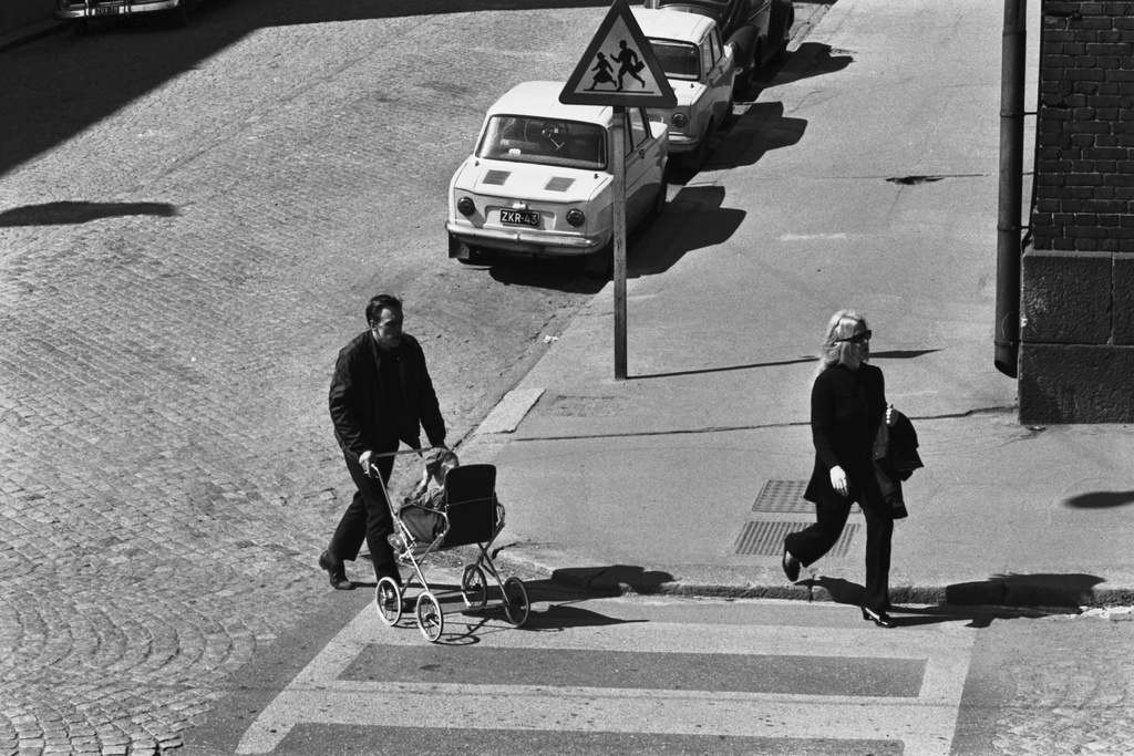 Porthaninkatu 7. Lastenrattaita työntävä mies sekä nainen ylittämässä katua Porthaninkadun ja Neljännen linjan risteyksessä, jossa lapsista varoittava likennemerkki.
