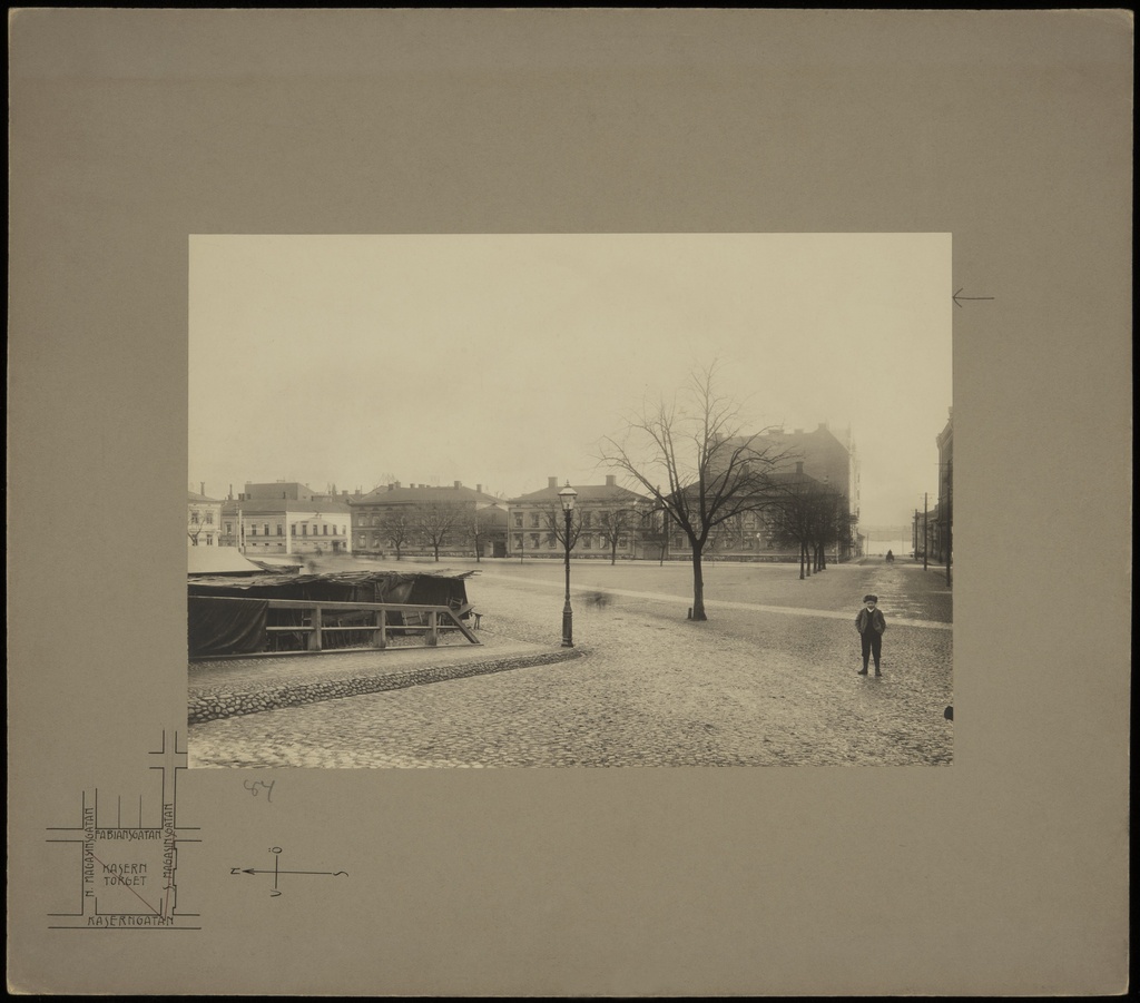 Näkymä Kasarmitorin yli itään, torin laidalla Fabianinkatu 13 (Eteläinen Makasiinikatu 5), 15, 17 ja 19 (Pohjoinen Makasiinikatu 5). Etualalla keskellä katulyhty ja oikealla poika.