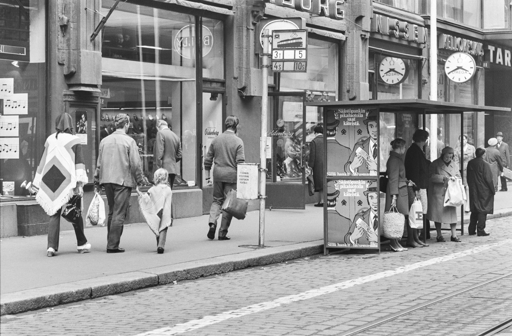 Aleksanterinkatu 11. Ihmisiä raitiovaunupysäkillä sekä muita jalankulkijoita Aleksanterinkadulla kävelykatukokeilun aikaan.