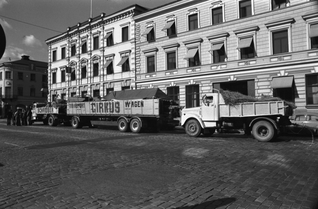 Pohjoisesplanadi. Sirkusautojen jono pysähtyneenä Pohjoisesplanadille. Taustalla Vanha apteekintalo, Pohjoisesplanadi 17, oikealla Helsingin kaupungintalo.
