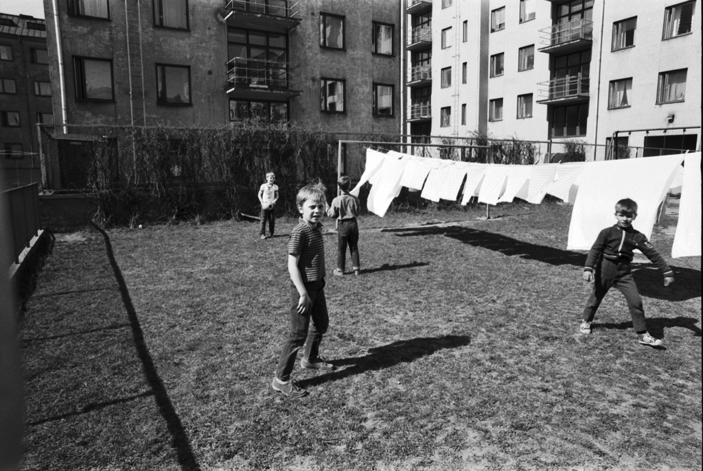 Neljäs linja 24. Pihanäkymä luoteeseen Kolmas linja - Castréninkatu - Neljäs linja - Suonionkatu -katujen ympäröimästä korttelista. Etualalla poikia pelaamassa jalkapalloa Neljäs linja 24:n nurmikkopihalla valkopyykin liehuessa narulla kuivumassa. Taustalla Neljäs linja 26.