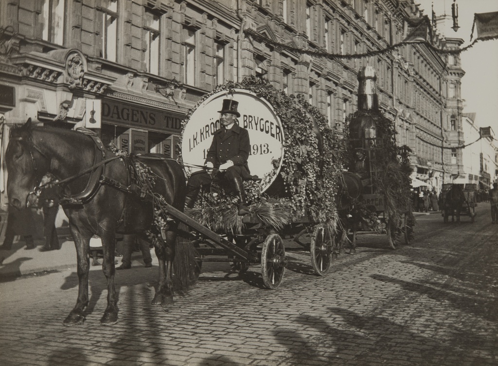 Juhlakulkue Pohjois Esplanaadikadulla (nyk. Pohjoisesplanadi) suomalaisen viikon (27.9.-4.10) aikaan vuonna 1913. Kulkueessa kaksi Pitäjänmäellä 1872 - 1921 toimineen J.K Kröckellsin panimoa mainostanutta hevosten vetämää kärryä, joista etummaisessa iso oluttynnyri ja taaemmassa iso portteripullo. Taustalla ns. Grönqvistin talo, Pohjoisesplanadi 25-27.