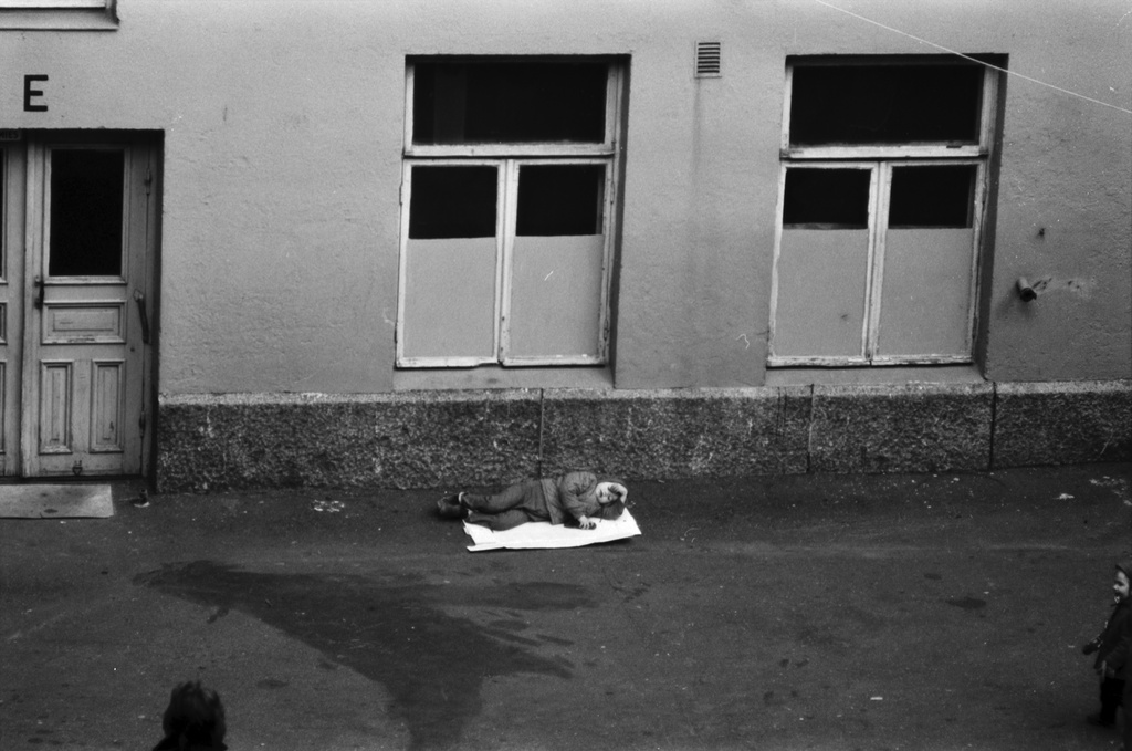 Liisankatu 7. Lasten leikkejä Liisankatu 7:n asfalttipihalla. Lapsi makaamassa pahvin palalla E-portaan viereisellä seinustalla. Kuva otettu B-portaan ikkunasta.