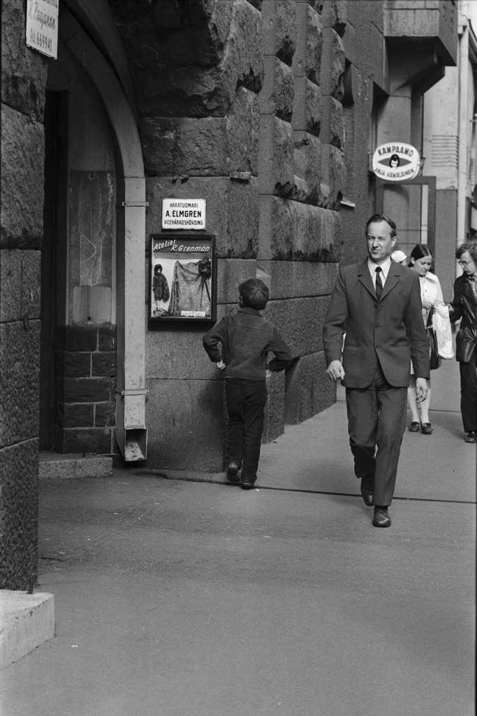 Poika ja muita jalankulkijoita Liisankatu 17:n kohdalla. Vasemmalla muotiateljee R. Grenmanin mainoskaappi.