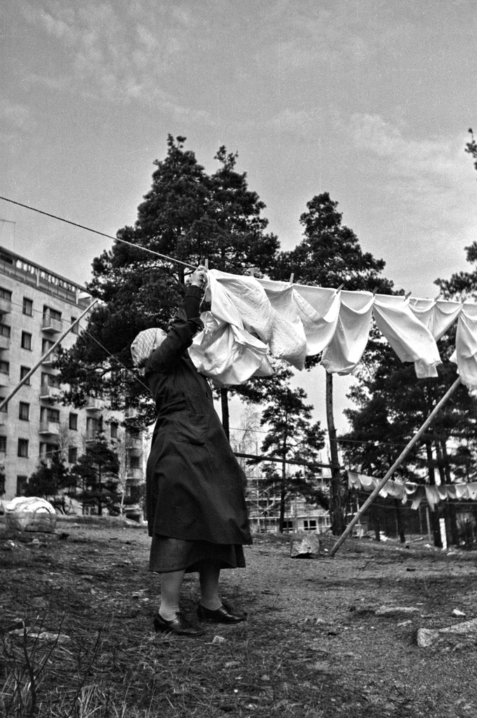 Nainen ripustaa pyykkejä narulle kuivumaan. Taustalla Mannerheimintie 118.