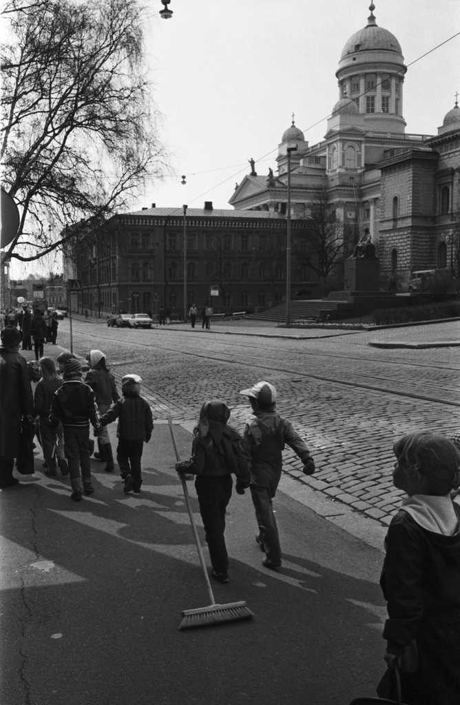 Snellmaninkatu. Vironniemen päiväkodin lapsia kävelemässä Snellmaninkadulla Rauhankadun kulmassa vappukarnevaalien harjakaisasuissaan. Keskellä tyttö vetää perässään asfaltilla pitkävartista siivousharjaa. Taustalla Tuomiokirkko.