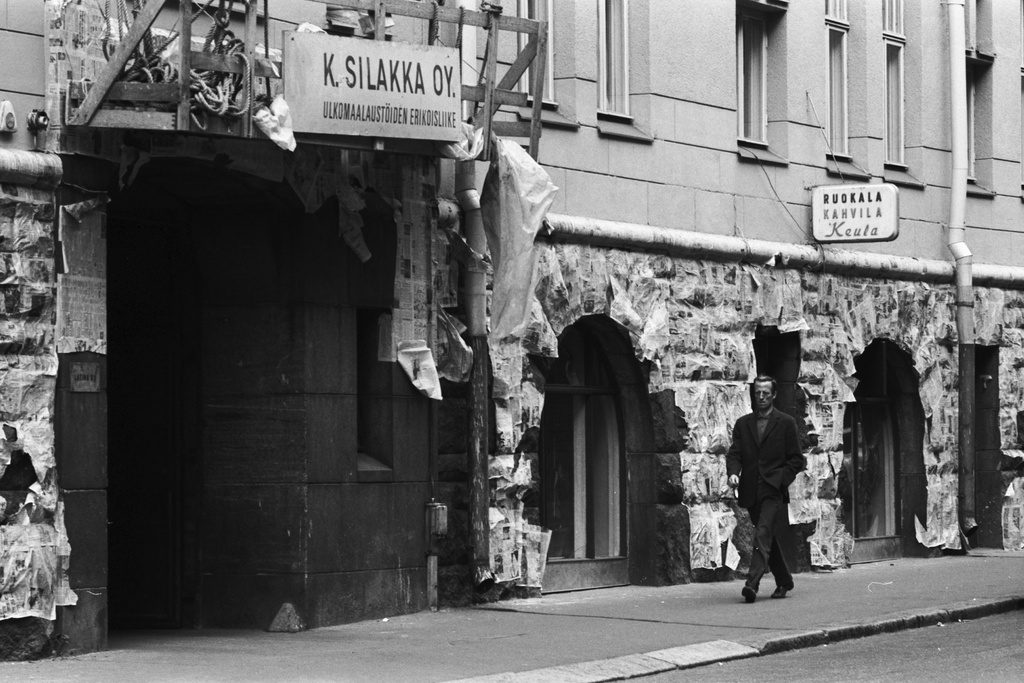Kruunuvuorenkatu 1. Kruunuvuorenkatu 1:n kerrostalon maalaustöiden ajaksi sanomalehdillä suojattu kivijalka. Porttikäytävän yläpuolella Ulkomaalaustöiden erikoisliike K. Silakka Oy:n maalarinkelkka. Oikealla Ruokala Kahvila Keulan kyltti.
