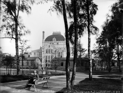 Kaisaniemen puisto, mies istuu penkillä. Vasemmalla joutsenlampi, taustalla Kansallisteatteri ja Villensaunan (Wilhelmsbad) kylpylän puurakennuksia.  duplicate photo