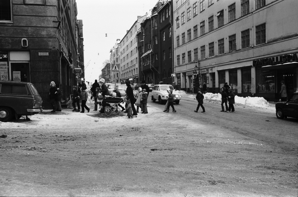 Kruununhaka, Liisankatu. Jonossa kulkevia lapsia sekä lastenvaunuja työntävä nainen ylittämässä Liisankatua Snellmaninkadun kulmassa. Vasemmalla olevassa kulmatalossa Elannon myymälä, oikealla olevassa Kansallis-Osake-Pankin konttori. Näkymä itään pain.
