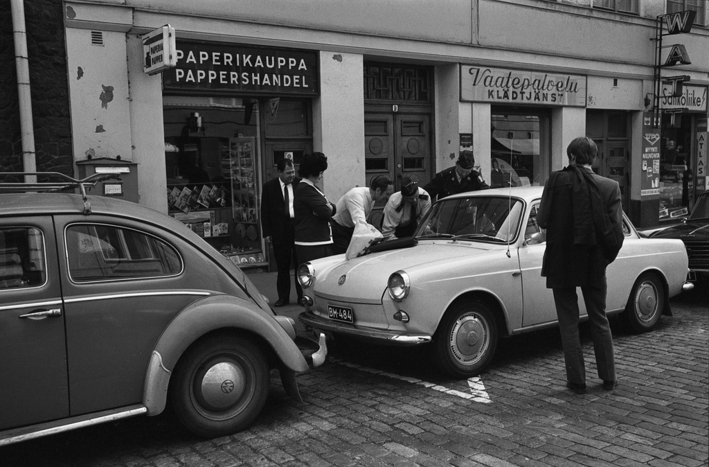 Liisankatu 18. Poliisit auttamassa ihmisiä auton oven avaamisessa Liisankadulla. Keskellä vaalea Volkswagen 1500 -henkilöauto. Vasemmalla Volkswagen, oikealla näkyy Peugeot 404.