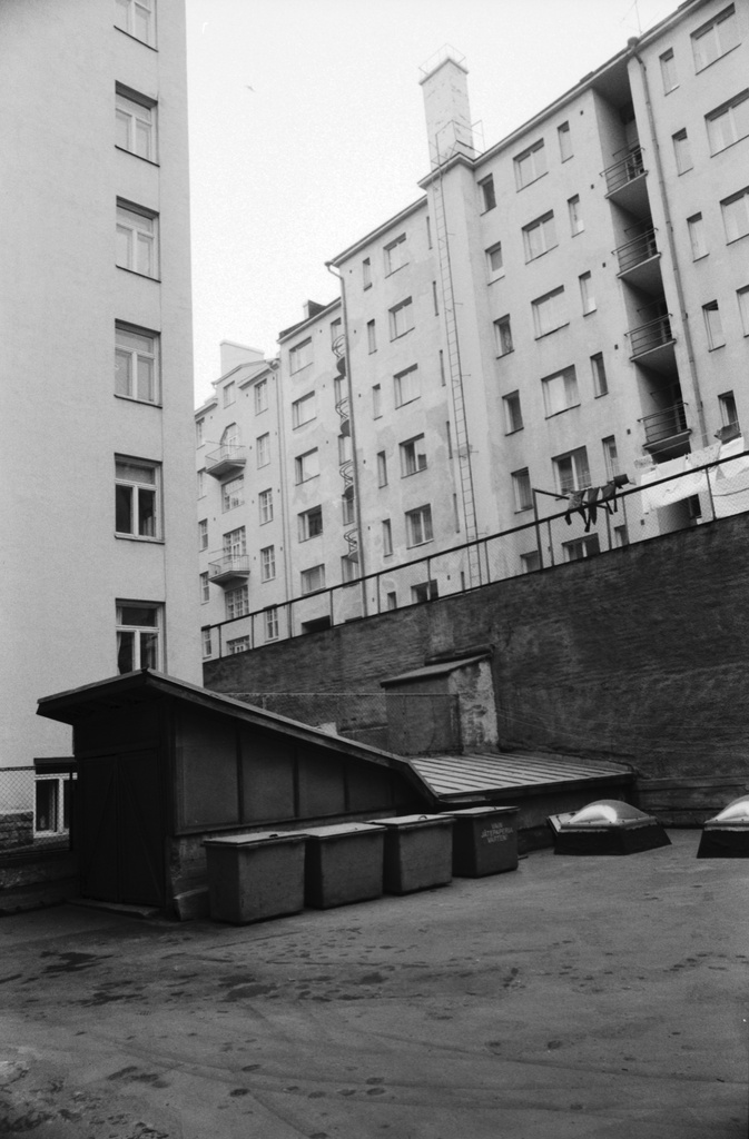 Kirjatyöntekijänkatu. Näkymä Kirjatyöntekijänkatu 8:n pihalta kaakkoon. Pihalla roskalaatikoita. Vasemmala Kirjatyöntekijänkatu 6:n talo. Oikealla ylätasanteella Kristianinkadun taloja.