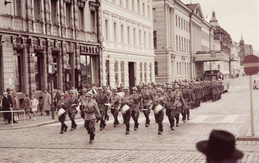 Vartioparaati Helsingissä marssimassa Pohjoisesplanadilla. Kaartin soittokunta ja pataljoona on juuri ohittanut Helsingin kaupungintalon ja saapuu Esplanadin puiston kohdalle.