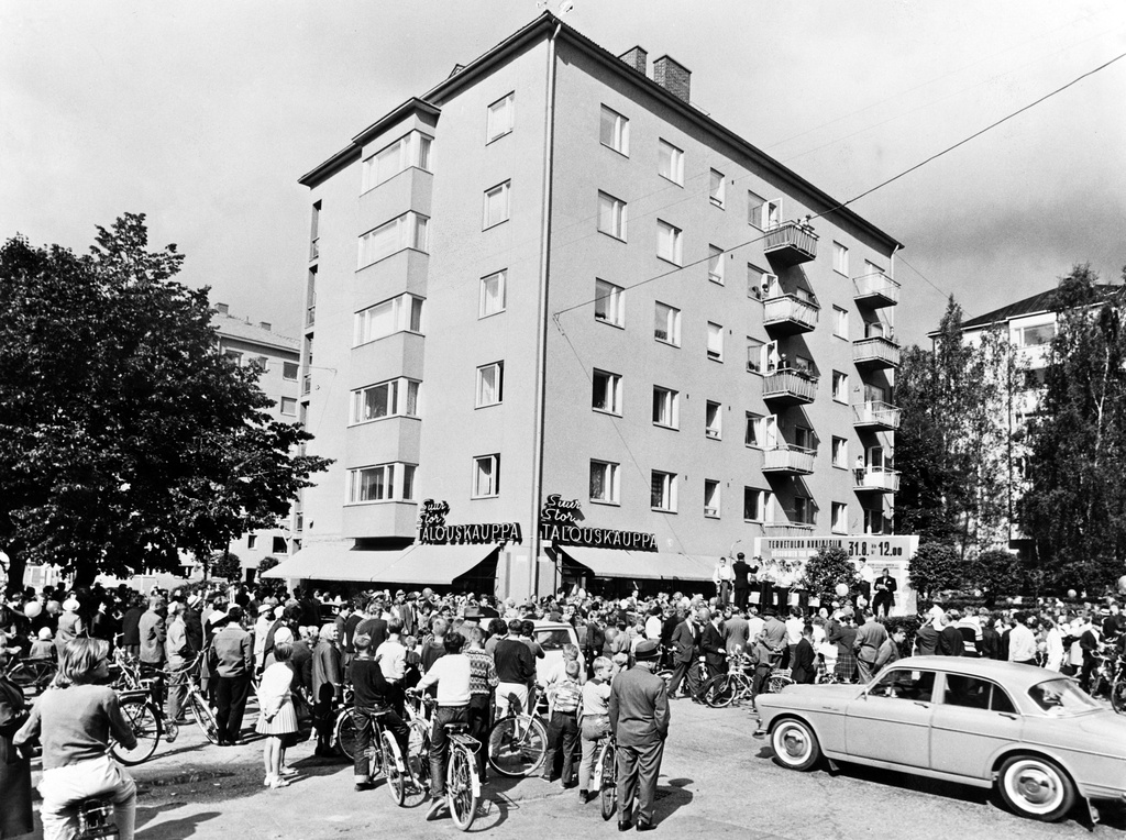 Talouskaupan myymälän nro 41 avajaiset Munkkiniemessä. Yleisöä kuuntelemassa avajaisjuhlan esityksiä. Oikeassa alakulmassa Volvo Amazon -henkilöauto.