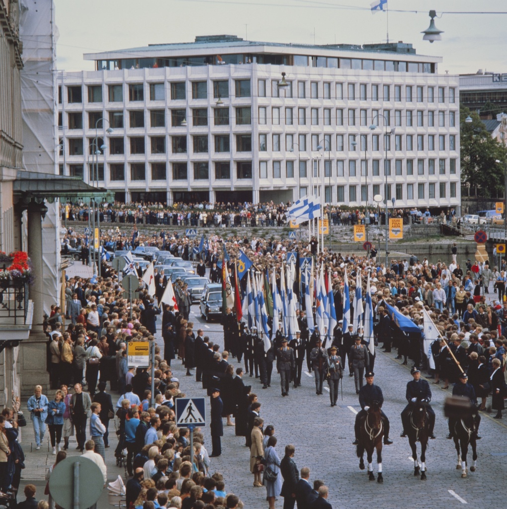 Presidentti Urho Kekkosen hautajaissaattue Pohjoisesplanadilla ohittamassa Presidentinlinnaa. Taustalla Enso Gutzeitin talo, Kanavaranta 1 - Kanavakatu 2.