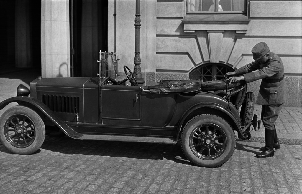 Henkilöauto Merikatu 5:n edustalla. Suojeluskunta-asuun pukeutunut mies täyttää vararengasta.