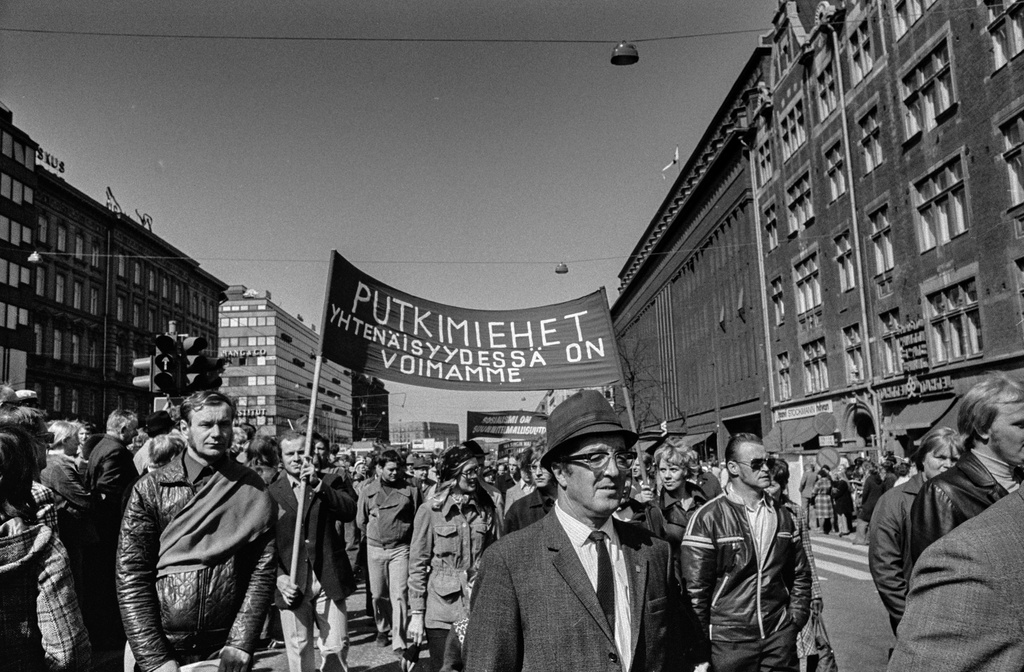 Vappumarssijoita Mannerheimintiellä Stockmannin tavaratalon kohdalla. Marssijat kantavat banderollia, jossa teksti: Putkimiehet yhtenäisyydessä on voimamme.