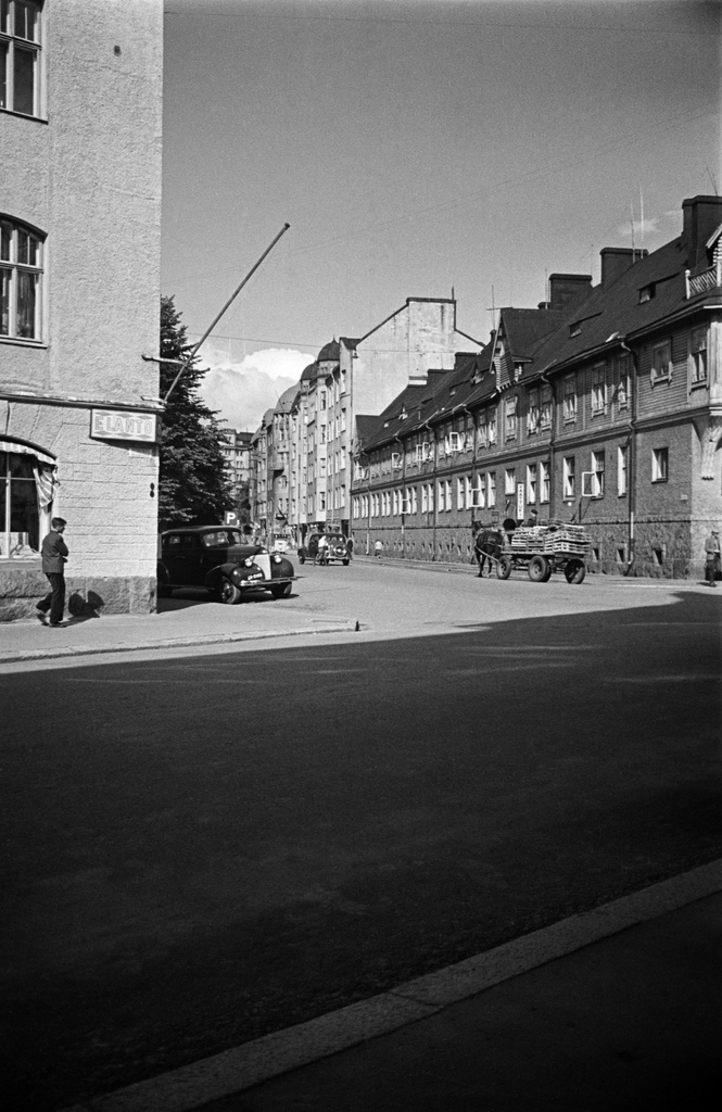Näkymä Pietarinkadulta pohjoiseen pitkin Kapteeninkatua, oikealla Kapteeninkatu 7, 9. Vasemmalla talon seinässä Elannon kyltti, oikealla vaatturiliike sekä hevosen vetämät kärryt. Auto vasemmalla Chevrolet, vuosimalli 1939.