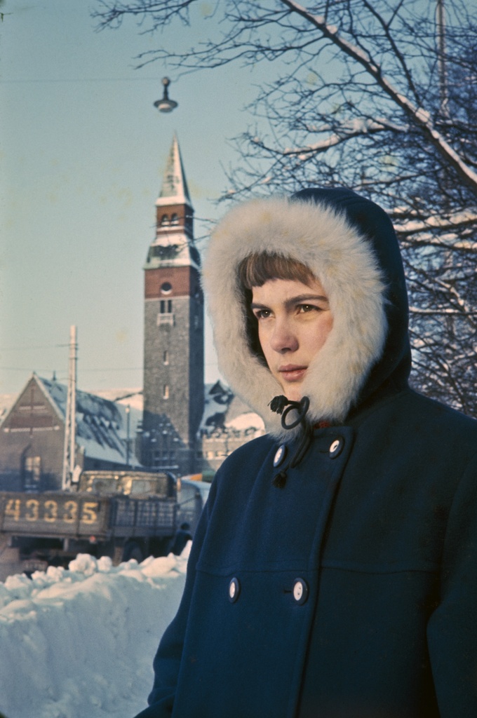 Nuori nainen seisoo Mannerheimintien varrella talvitakissa ja katsoo kohti laskevaa aurinkoa. Hänen vasemmalla puolellaan näkyy Kansallismuseon torni ja sivulaiva. Nainen on pukeutunut tummansiniseen talvitakkiin, jonka hupussa on tuuhea vaaleakarvainen reunus. Hänen takanaan kuvan oikeaa reunaa peittää lehtipuiden paljaat oksat. On talvi, ja kadunreunaa pengertävät korkeanpuoleiset kinokset. Kadulla museorakennuksen ja kuvauspaikan välissä näkyy kuorma-auto, jonka lavan takaluukkuun on maalattu numero 43335.