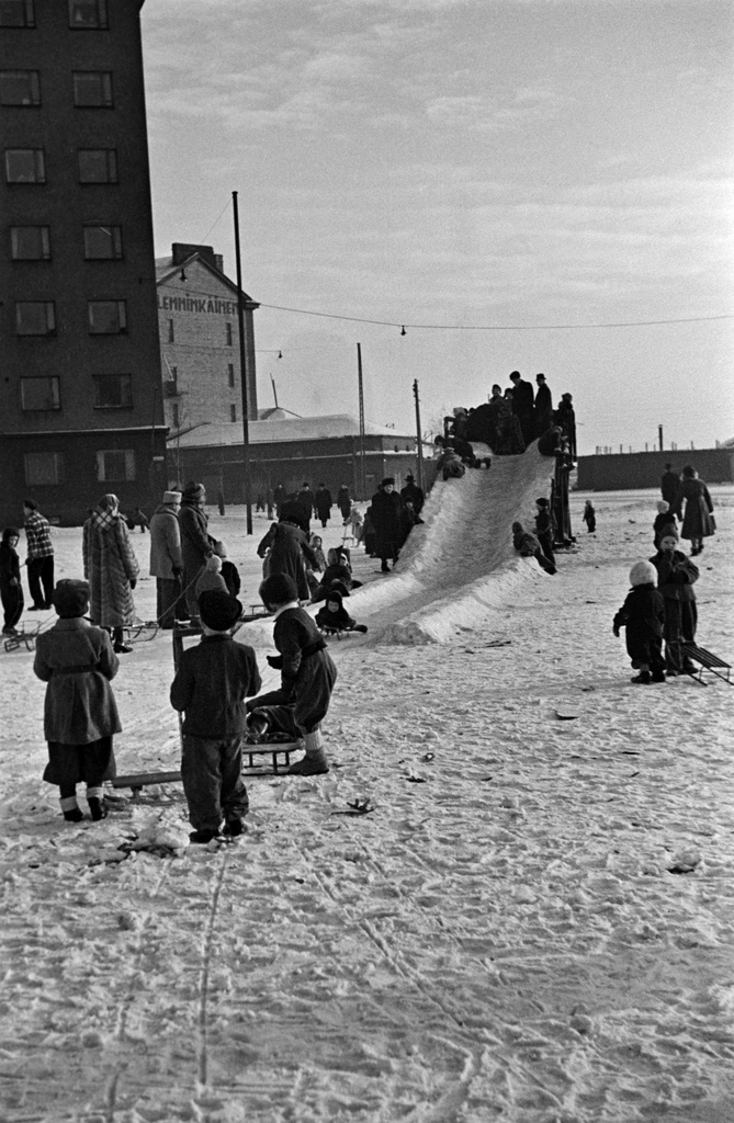 Jäämäki ja lapsia laskemassa mäkeä Hakaniementorin kaakkoiskulmassa. Taustalla Viherniemenkatu 1 ja Hakaniemenkatu 2.