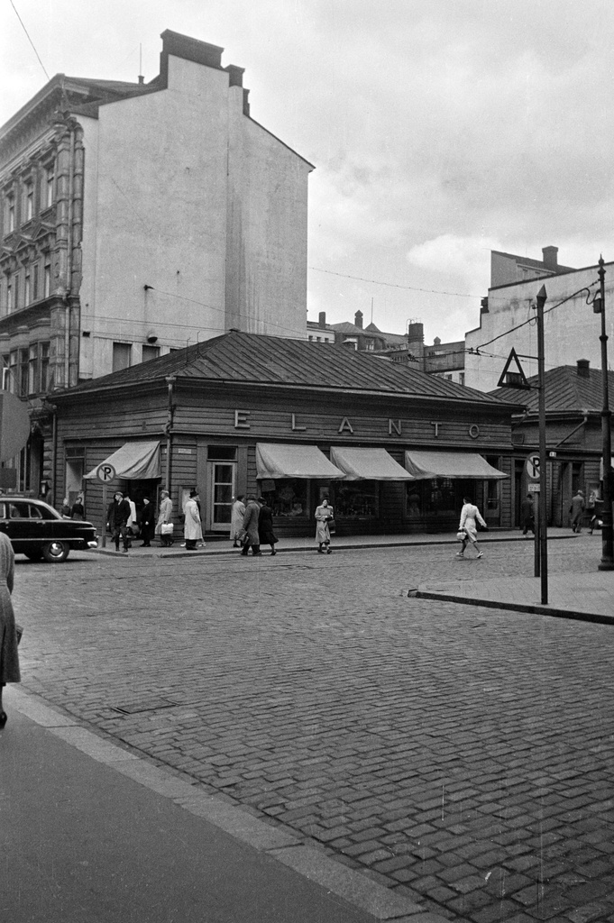 Aleksanterinkatu 9. - Kluuvikatu 5 Kluuvikadun suunnasta nähtynä. Elannon myymälä ja Elannon suur-aitta. Puurakennukset purettiin syksyllä 1950 ja paikalle rakennettiin Elannon tavaratalo.