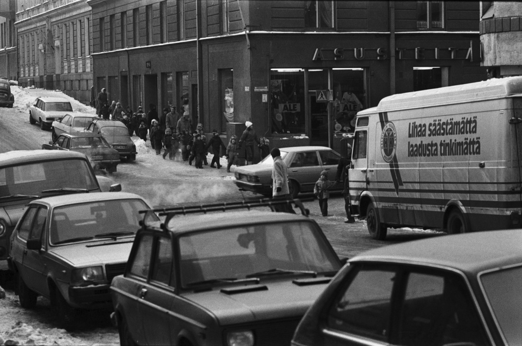 Meritullinkatu. Vironniemen päiväkodin väki autojen keskellä ylittämässä jonossa Liisankatua ja Meritullinkatua. Ollaan matkalla tutustumaan Liisankatu 7 - Meriullinkatu 25-27 - taloon, jossa muutamat lapset asuivat. Tutustumiskäynti liittyi päiväkodissa kevätkaudella toteutettuun Viihtyisä ympäristö -projektiin.