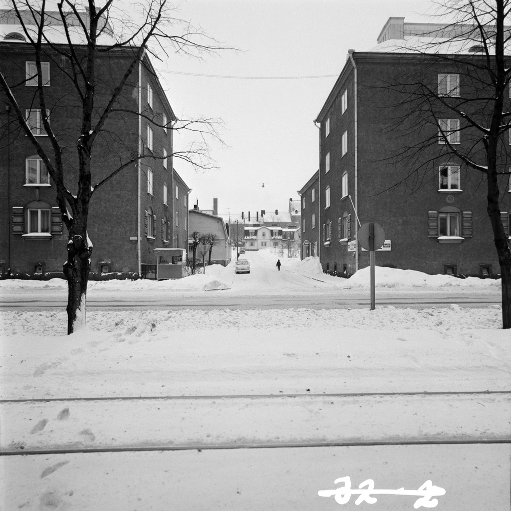 Näkymä Mäkelänkadun ja Ähtärintien kulmasta koilliseen kohti Inarintietä. Mäkelänkatu 21:n tontilla todennäköisesti nakkikioski. Kuvan etualalla raitiotiekiskot.