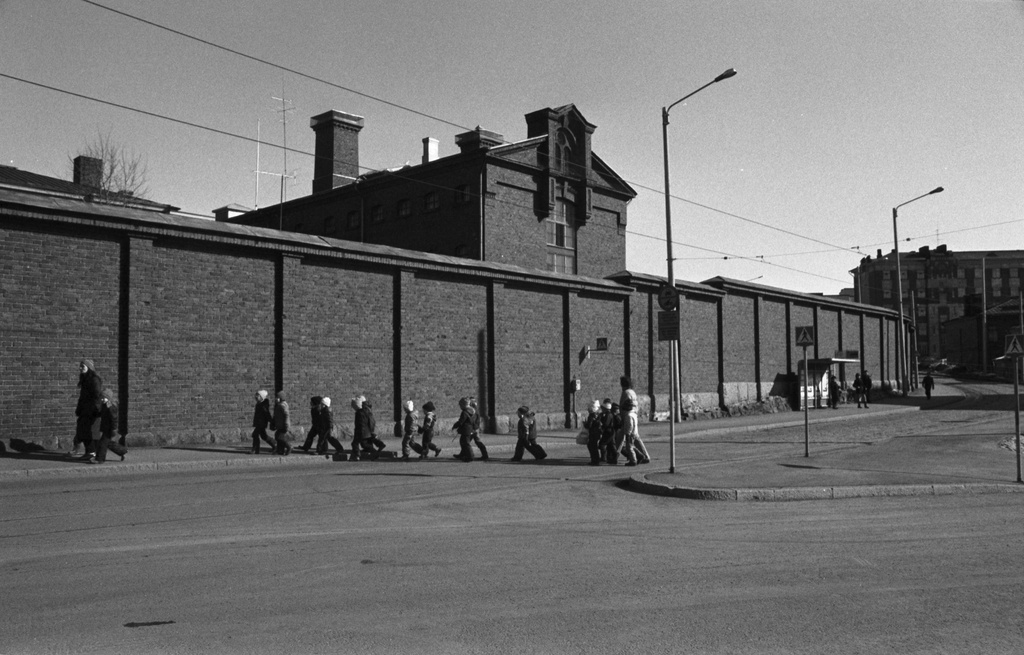 Linnankatu. Vironniemen päiväkodin lapsia ja aikuisia kävelemässä Katajanokan vankilan muurin vierustalla Katajanokan tutustumiskierroksella. Näkymä koilliseen Merikasarminkadun suuntaan.