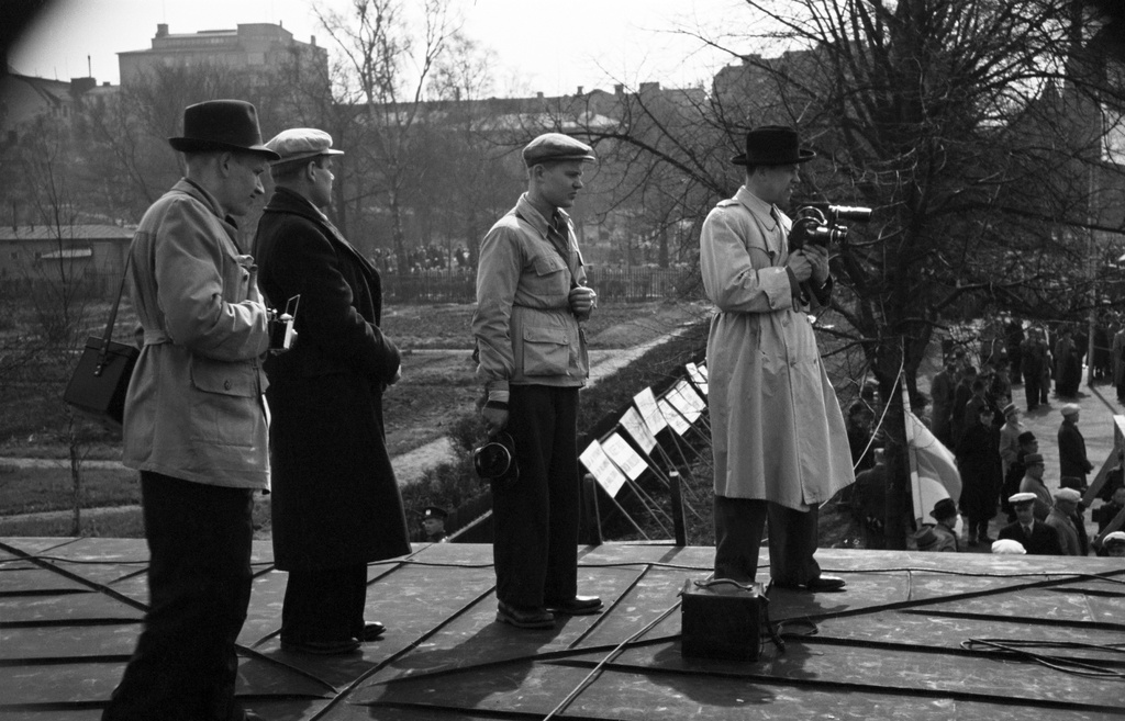 Vappujuhla Kaisaniemen kentällä. Kuvaajia rakennuksen katolla, taustalla juhlijoita ja tekstikylttejä.