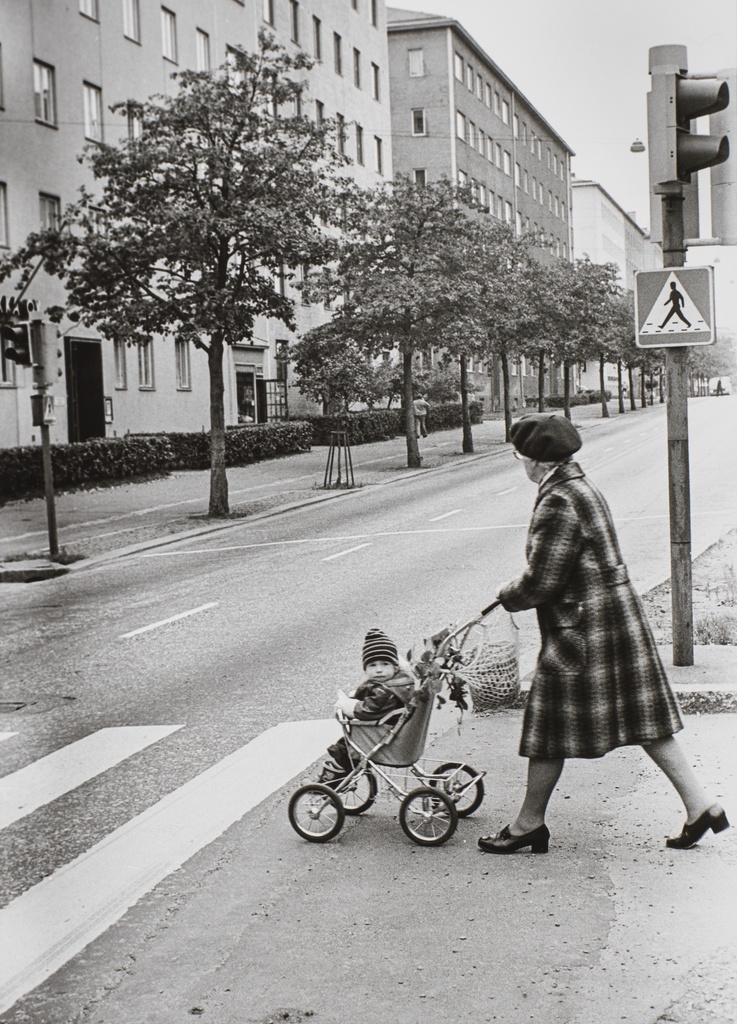 Jalankulkija työntää lastenrattaita suojatiellä Mannerheimintien ja Jalavatien risteyksessä. Taustalla Mannerheimintie 134, 136, 138.