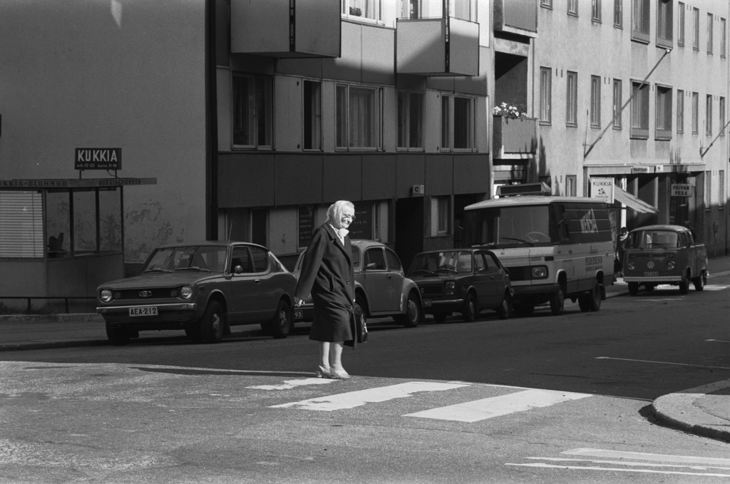 Punavuorenkatu. Iäkäs nainen ylittämässä Punavuorenkatua Albertinkadun kulmassa. Vasemmalla kukkakioski, taustalla Punavuorenkatu 7.