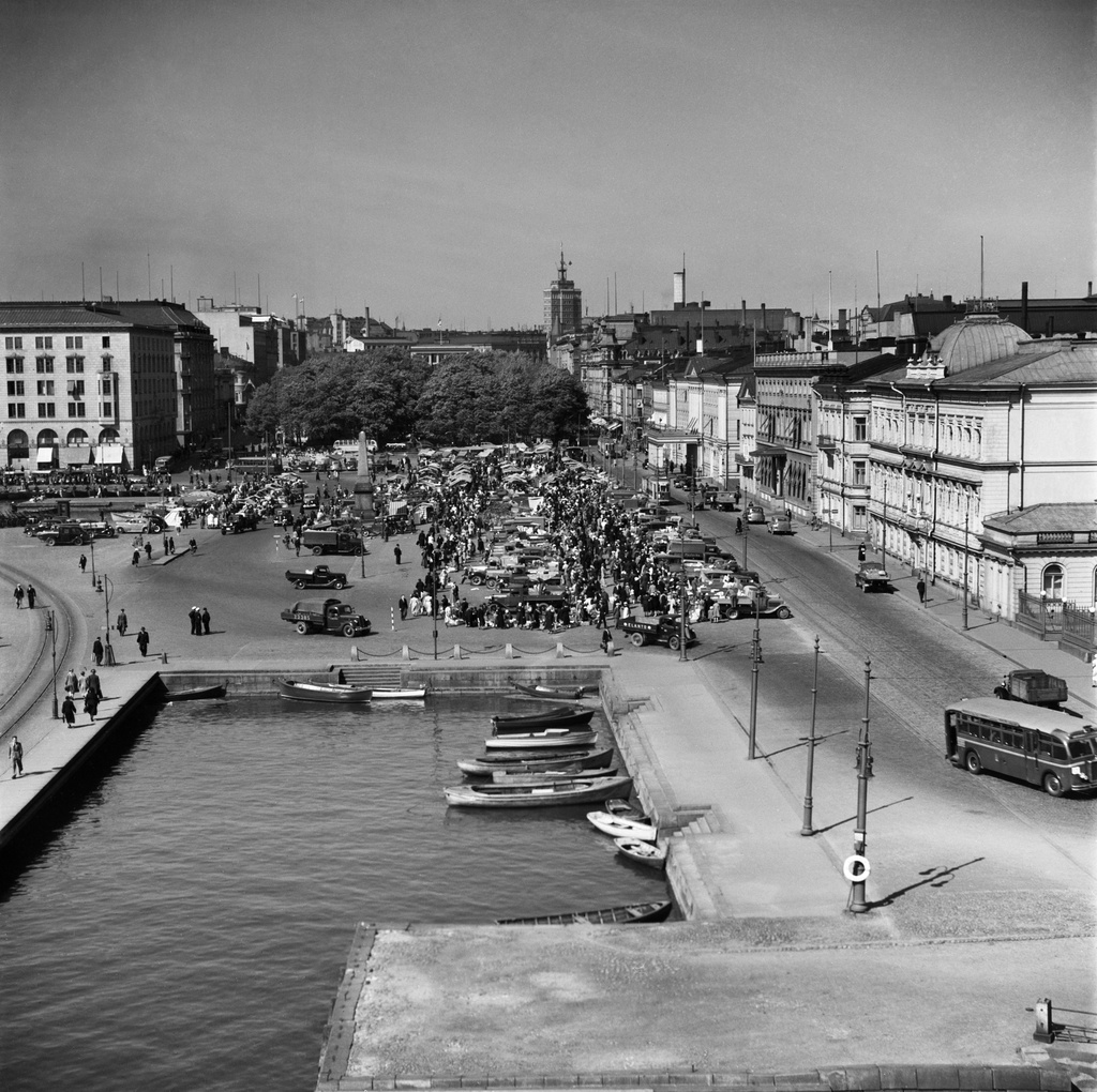 Kauppatori, yleiskuva. Torikauppaa. Kuvattu Linnanaltaan takaa länteenpäin. Vasemmalla Eteläesplanadi 2, 4, 6, 8, 10. Oikealla Pohjoisesplanadi 3, 5, 7, 9, 11, 13, 15, 17, 25. Taustalla Hotelli Torni.