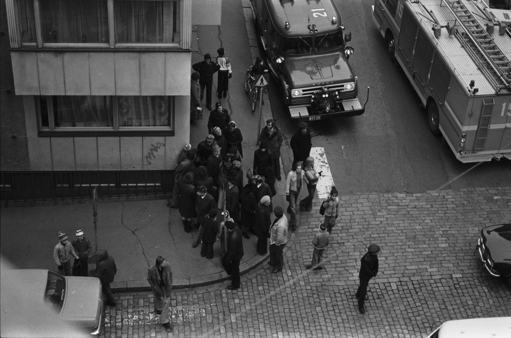 Liisankatu 4. Meritullinkatu. Pelastusmiehistö valmistautuu Meritullinkatu 20:n katolle kiivenneen miehen pelastustoimiin. Ihmisiä seuraamassa kadulla tapahtumaa Liisankadun ja Meritullinkadun kulmassa. Kuvattu Liisankatu 7:n neljännen kerroksen ikkunasta.