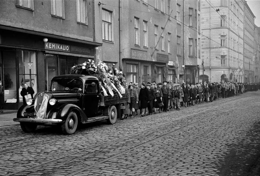 Miina Sillanpään hautajaiset, hautasaatto Lapinlahdenkatu 9:n, 7:n ja 3:n kohdalla. Kulkueen edessä hautaseppeleitä kuljettava auto.