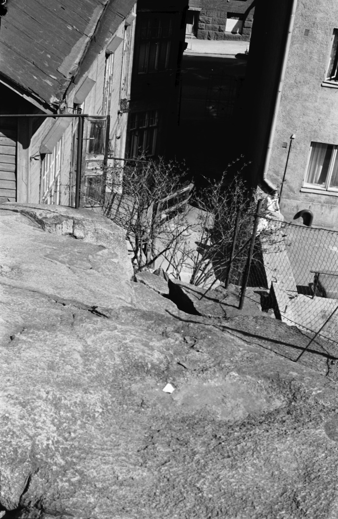 Fleminginkatu 16. Näkymä kalliolta Fleminginkatu 16:n pihalta kadun suuntaan. Oikealla Fleminginkatu 14:n talon pääty. Taustalla Fleminginkatu 15:n kivijalkaa.