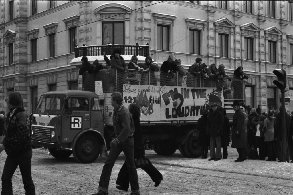 Pohjoisesplanadi. Abiturienttien perinteinen penkinpainajaispäivän ajelu. Abeja plakaatein koristellun kuorma-auton lavalla Pohjoisesplanadin ja Unioninkadun kulmassa. Taustalla Vanha apteekintalo.
